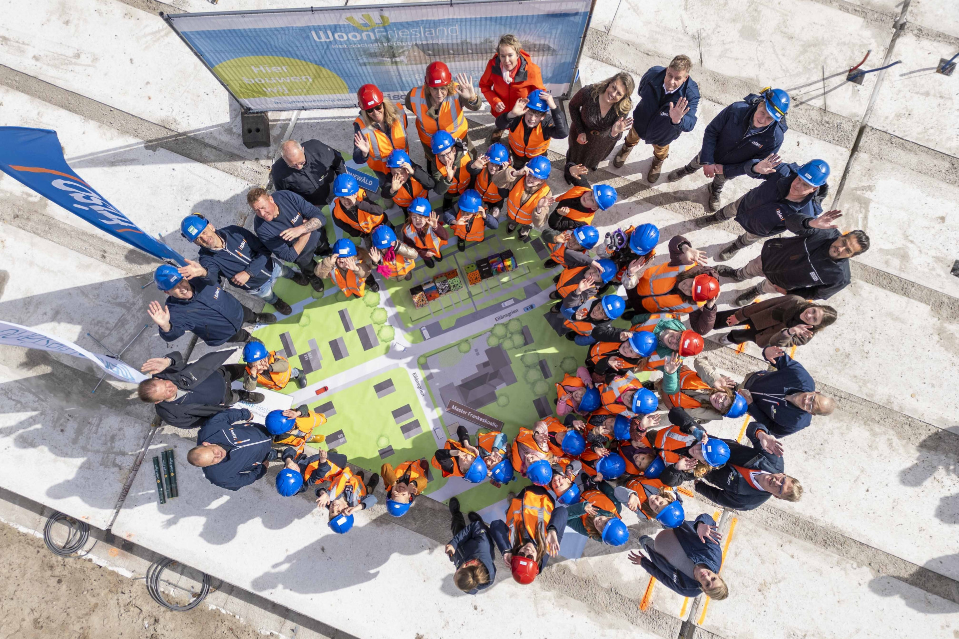 Groep bouwmedewerkers en kinderen verzamelen rondom het bouwplan in Earnewâld.