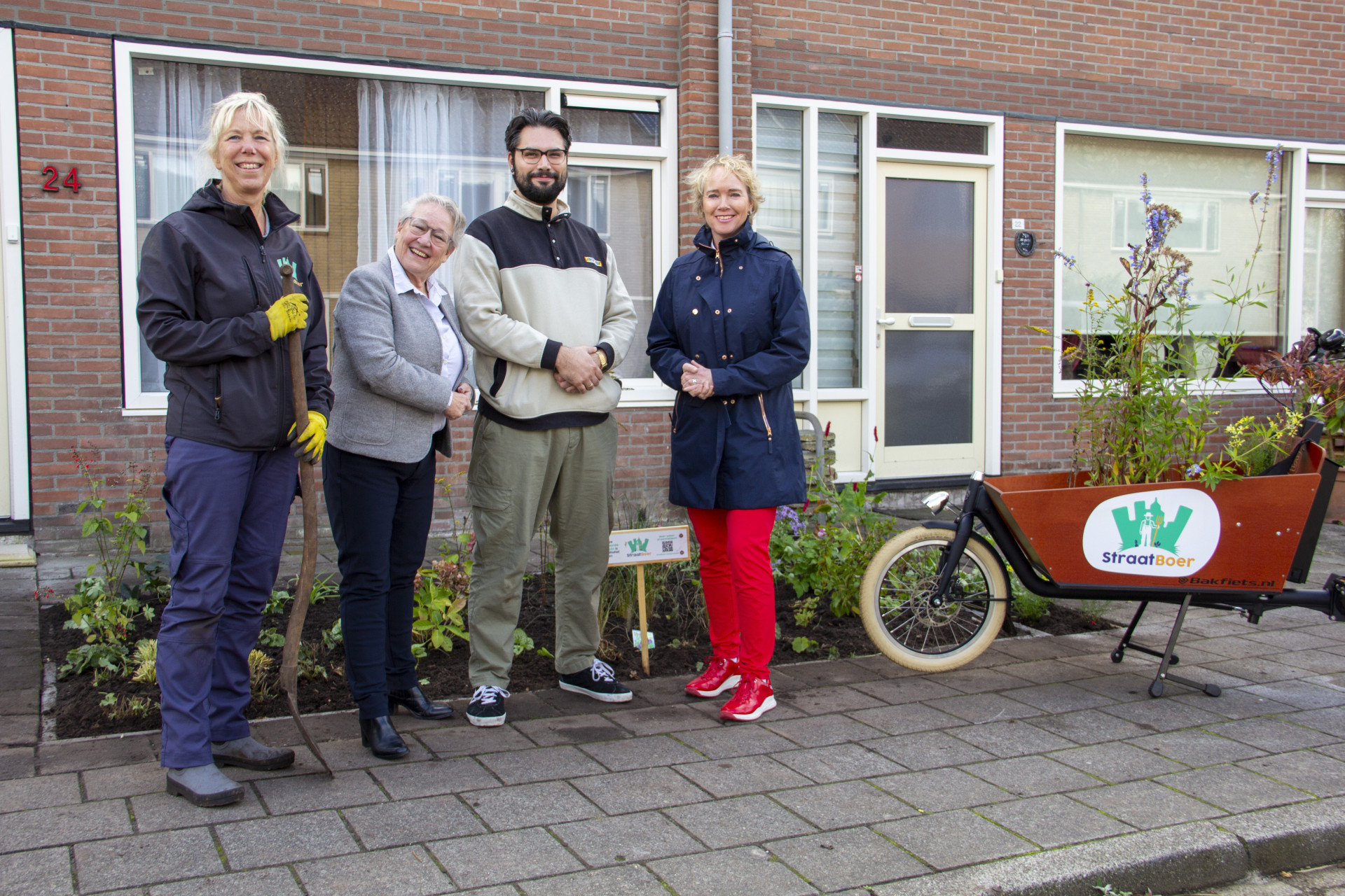 Wethouder Maria le Roy en directeur-bestuurder Sigrid Hoekstra poseren samen met Stichting Straatboer en een trotse bewoner bij een groene voortuin in Drachten.