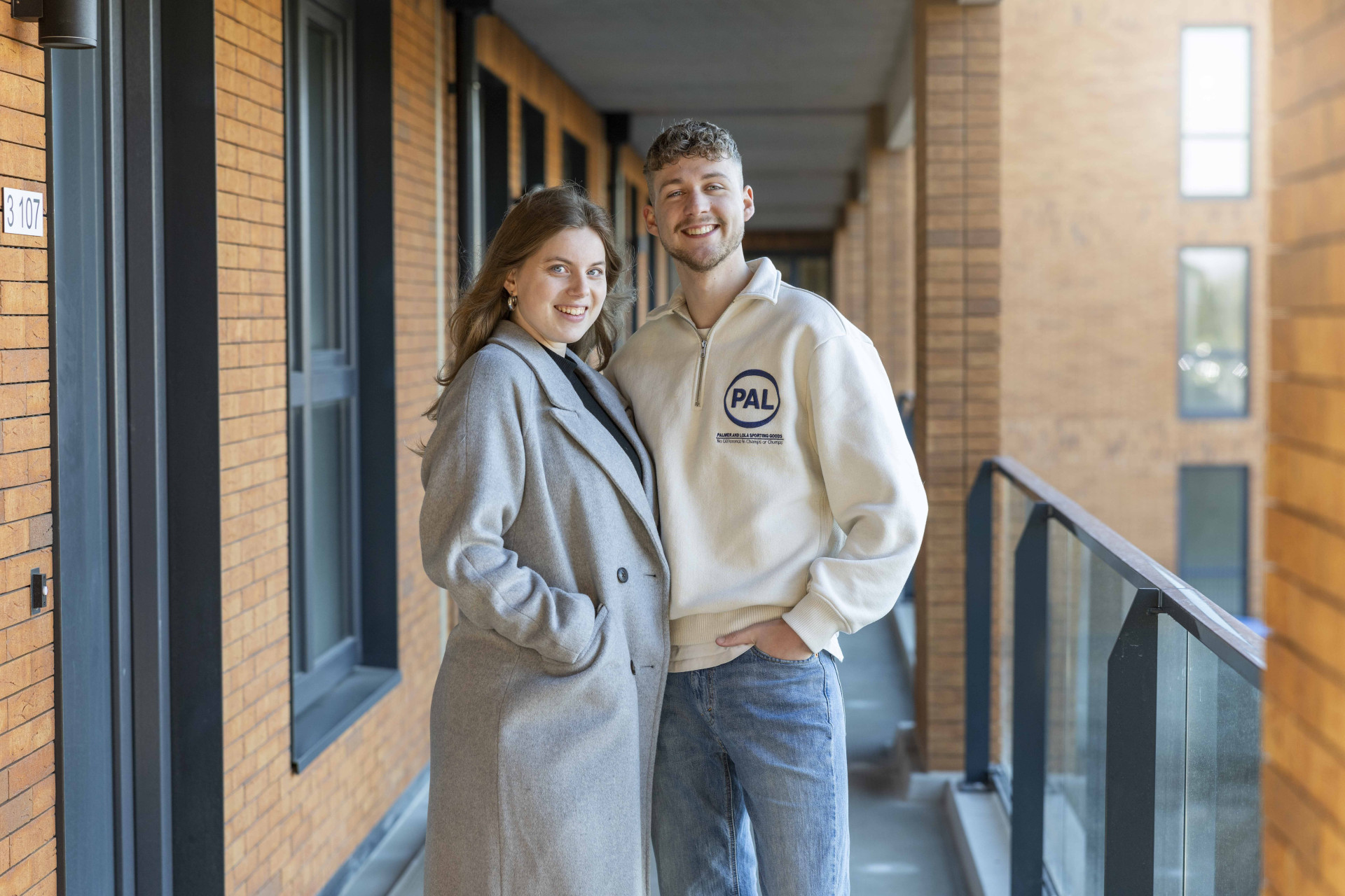 Twee jonge bewoners poseren bij de voordeur van hun nieuwbouwappartement in It Skûlplak in Sneek.