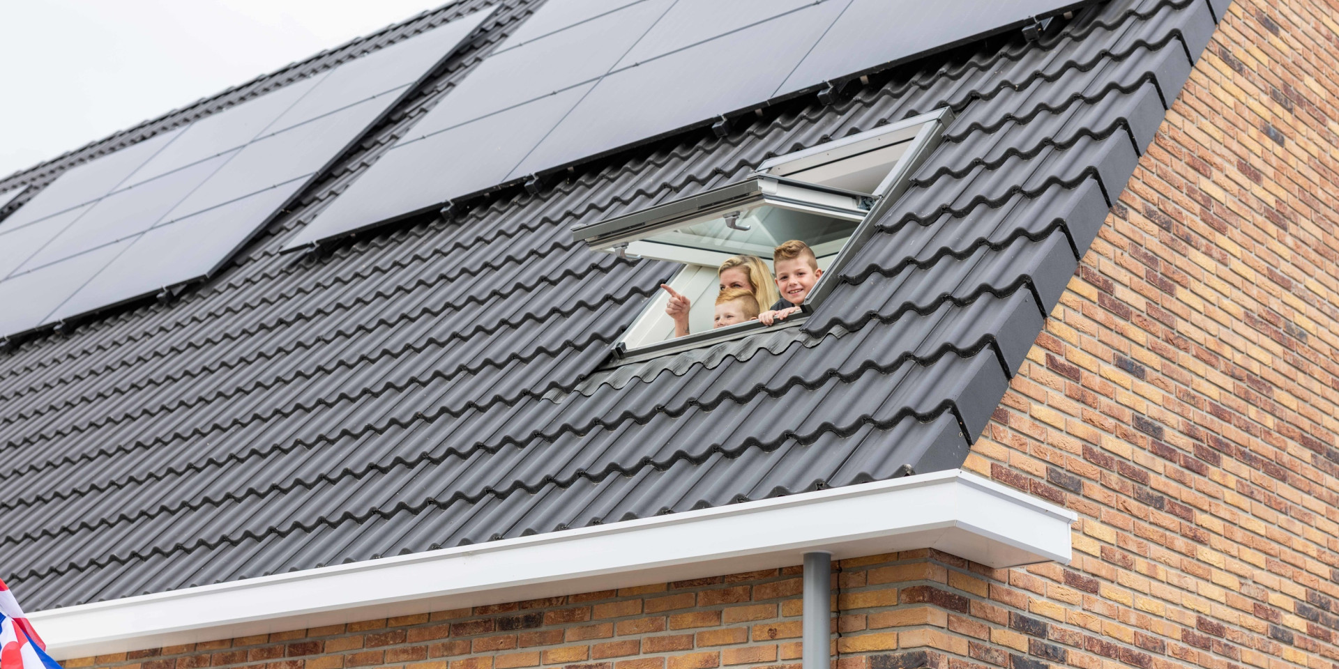 Een gezin kijkt naar buiten door een raam in het dak, met zonnepanelen op het dak.